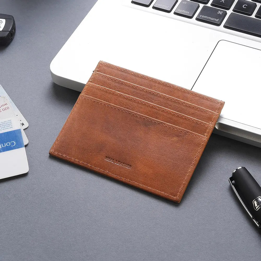 Cognac leather card holder on a gray surface with a laptop and cards in the background