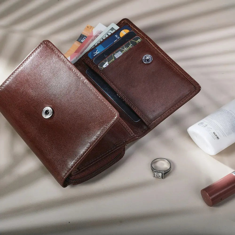 Cognac leather wallet with cards, ring, and lip gloss on a light surface
