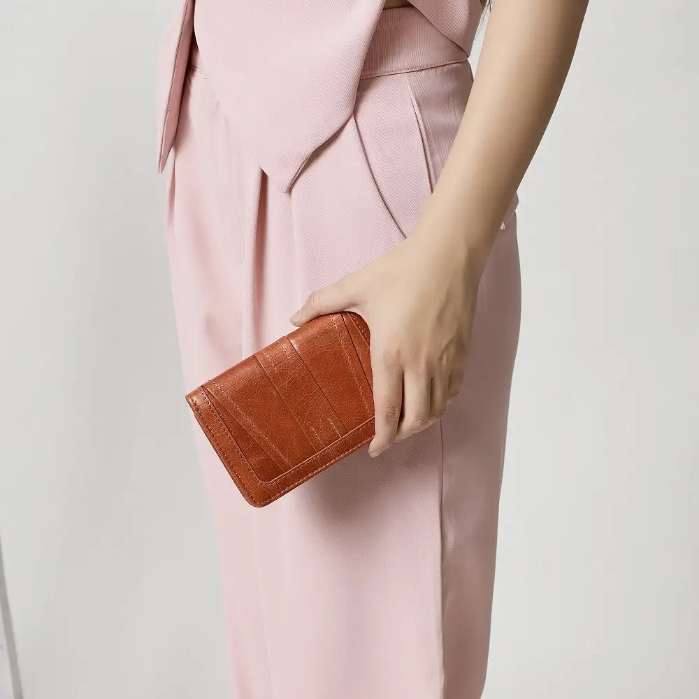 Person holding a cognac leather purse against a light pink background