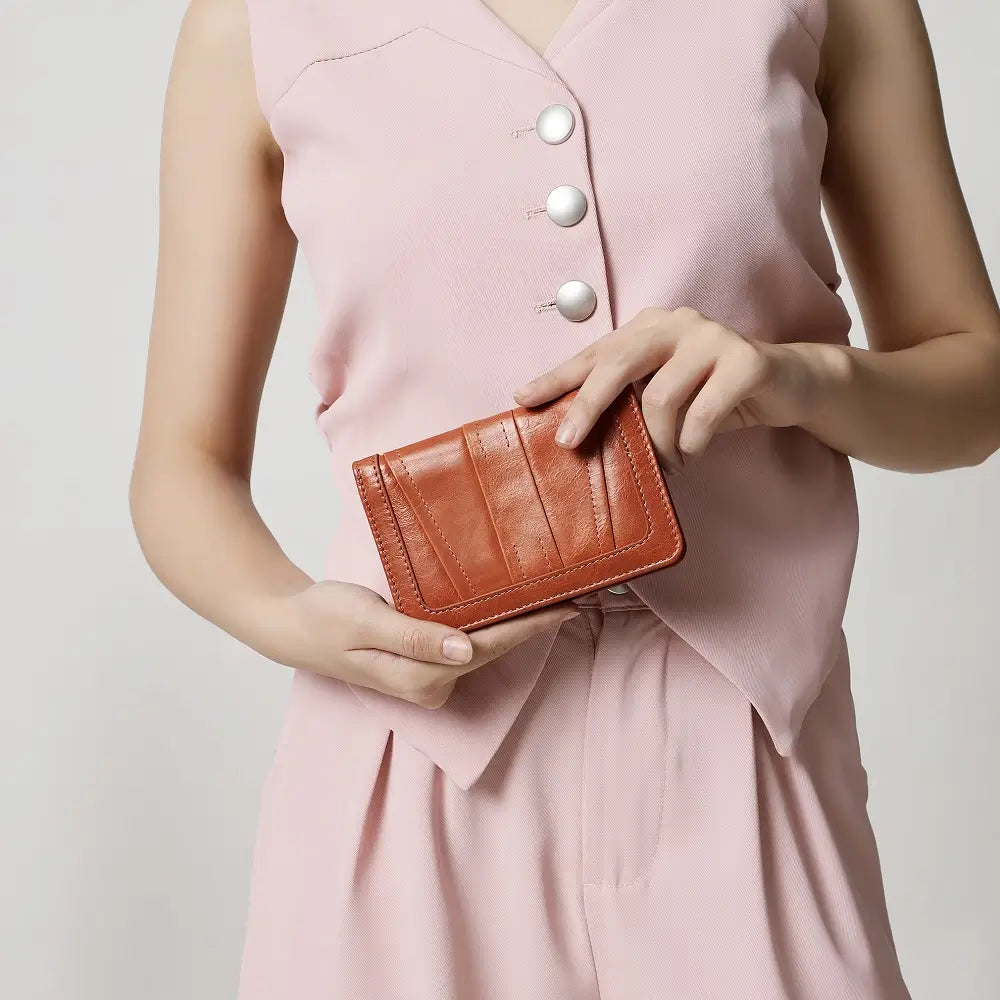 Person holding a cognac leather purse against a light pink background