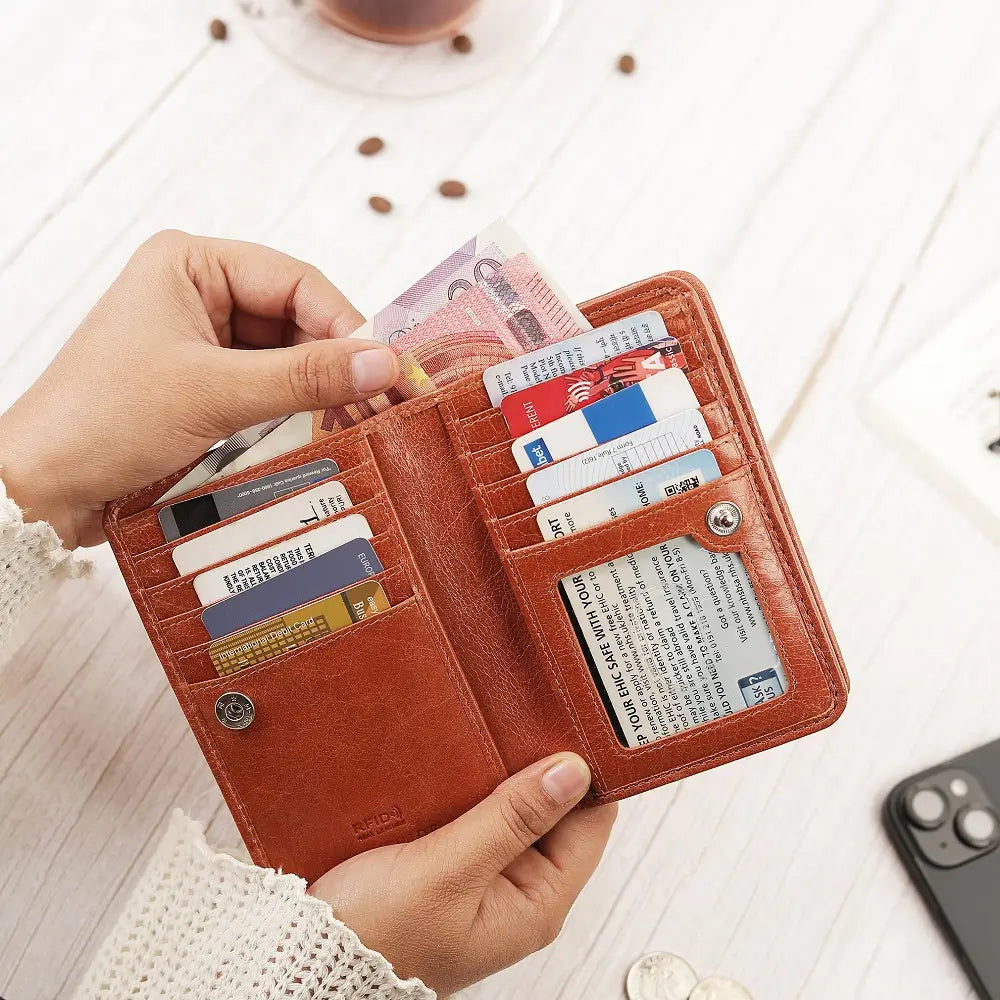 cognac leather purse with cards and money held by a hand on a light wooden surface.