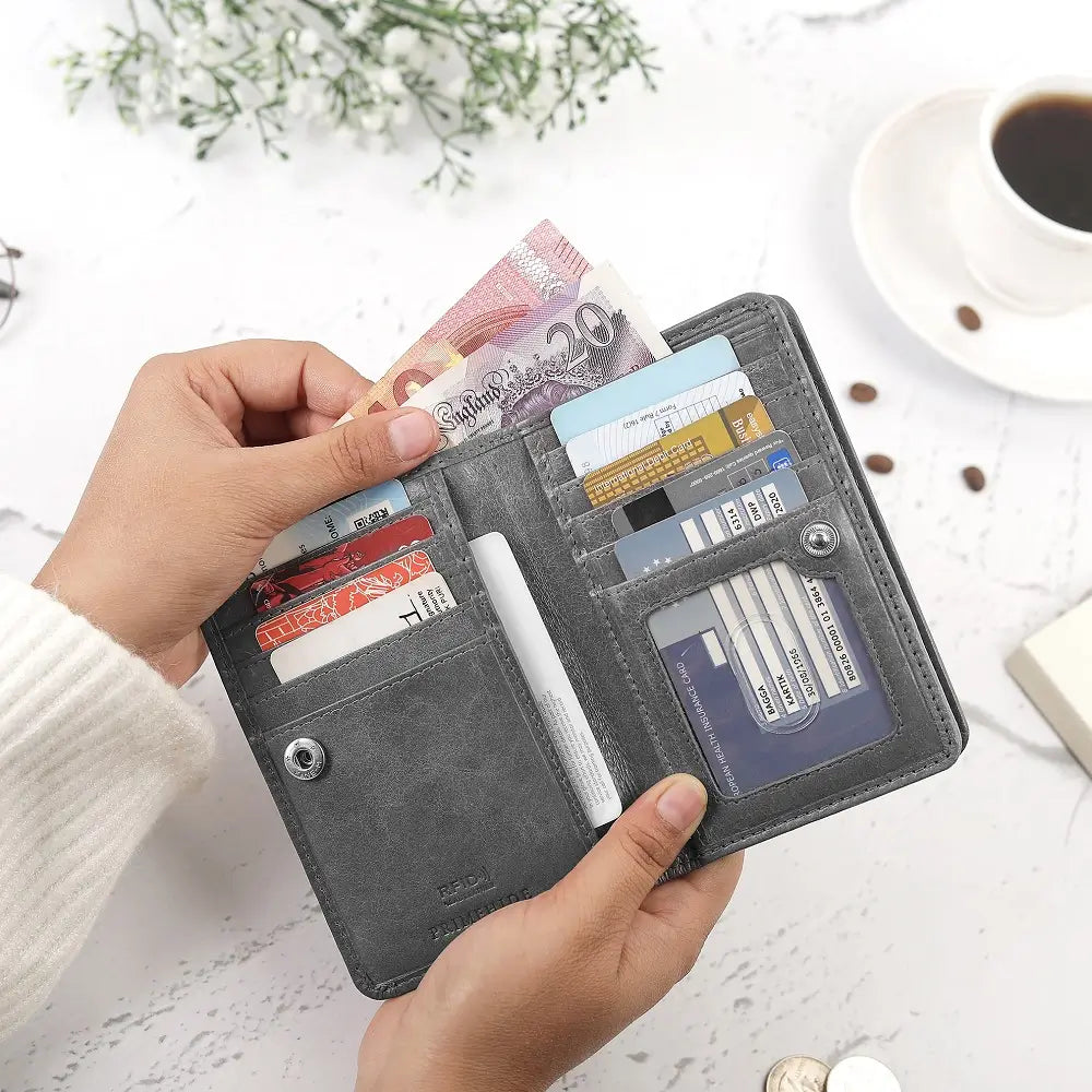 Person holding a Grey Purse with money and cards on a light surface with a cup of coffee and flowers.