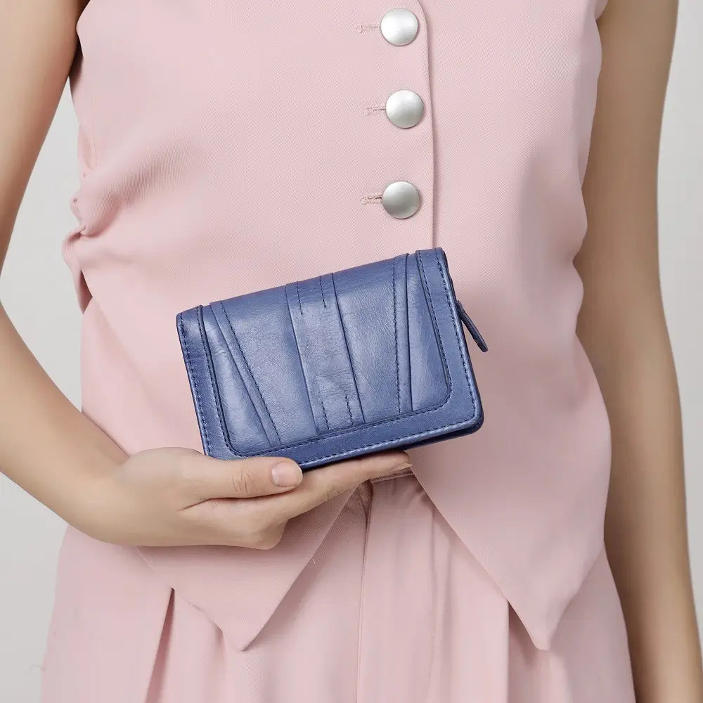 Person holding a Grey Purse against a light pink dress with silver buttons.