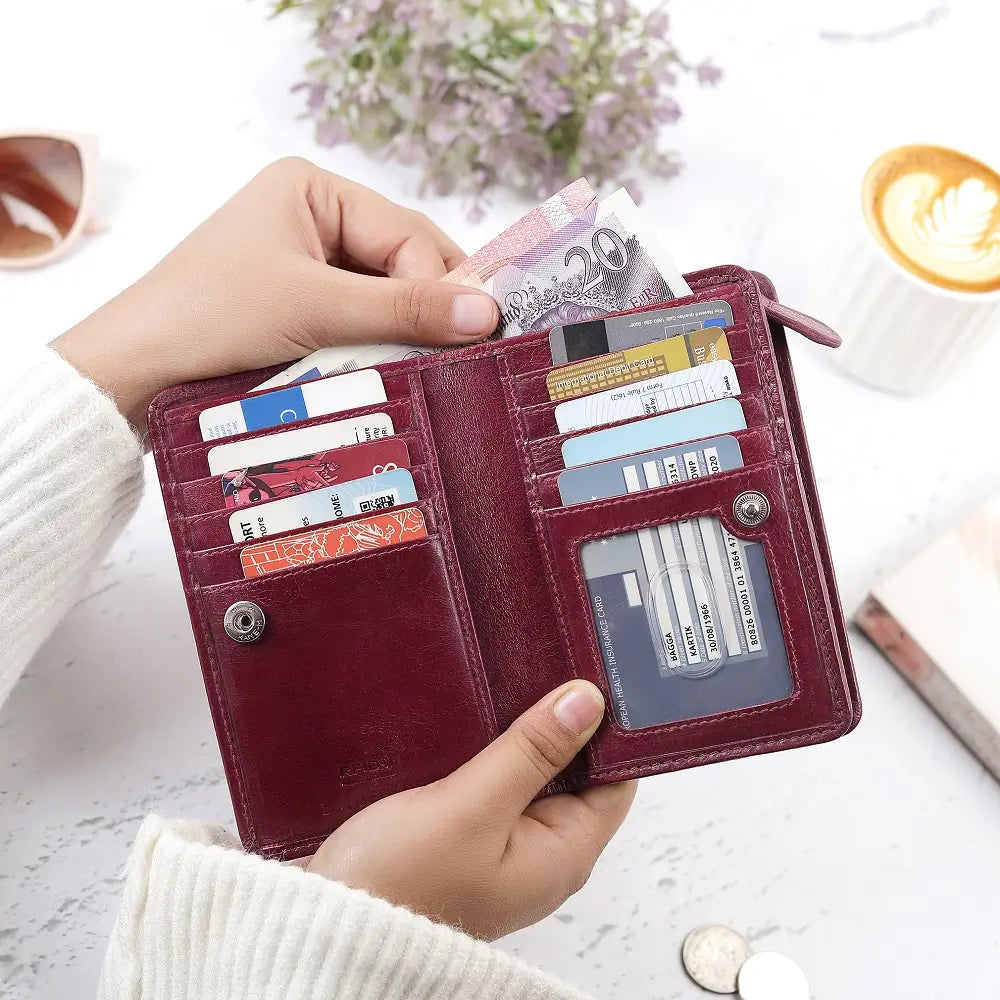 Person holding a Maroon purse  with cards and money, with a blurred background of a cup of coffee and flowers.