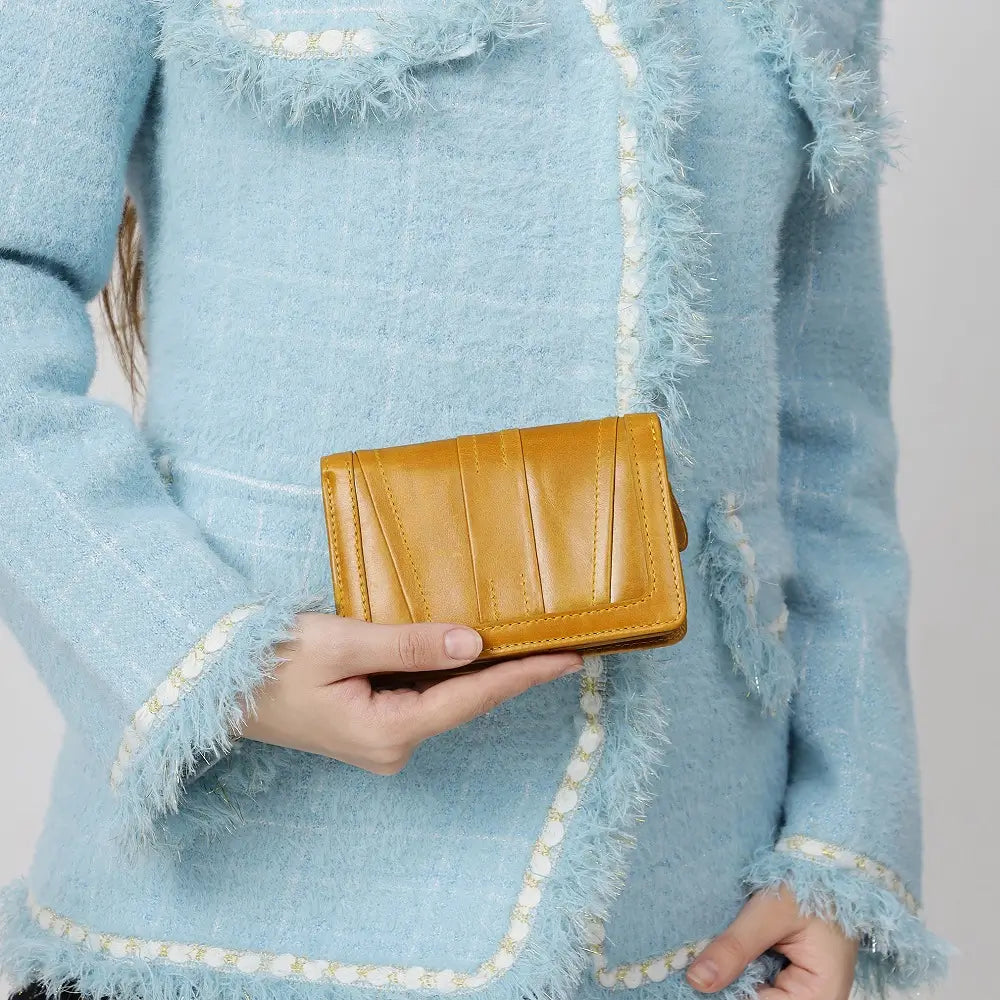 Person wearing a light blue textured coat holding a Mustard Purse.