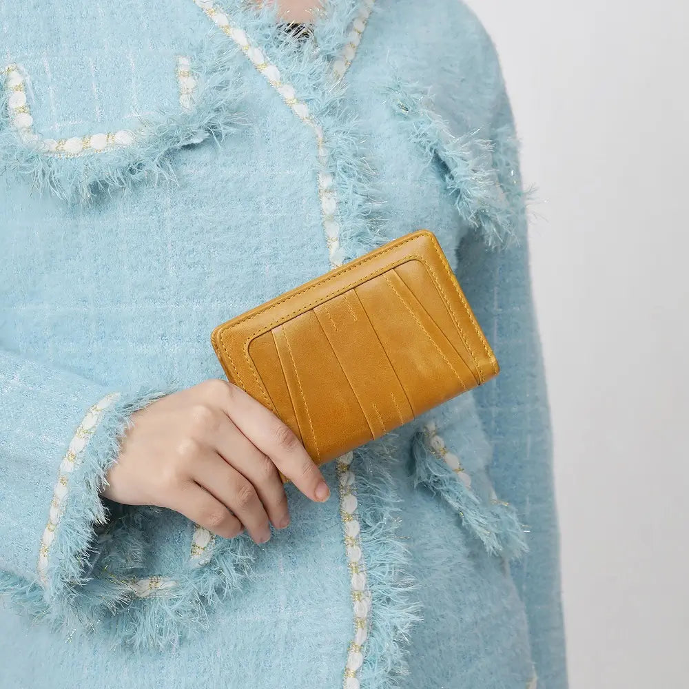 Person wearing a light blue textured coat holding a Mustard Purse.