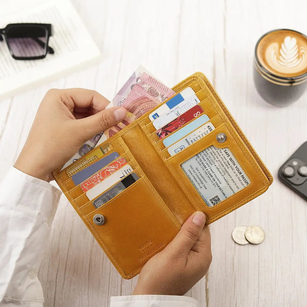 Person holding a Mustard Purse with cards and money on a light wooden surface.