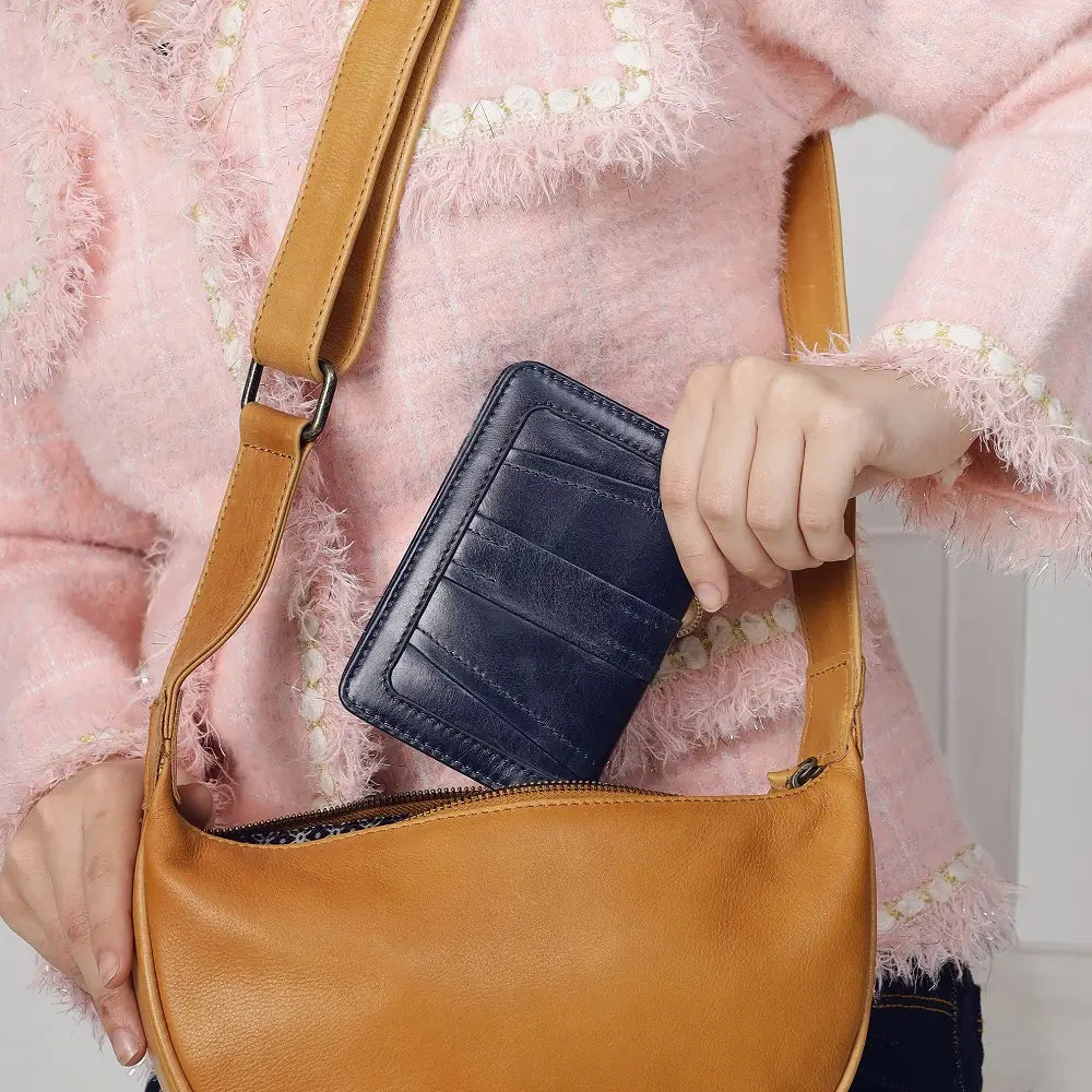 Person holding a brown leather bag with a black purse  inside, wearing a pink textured sweater.