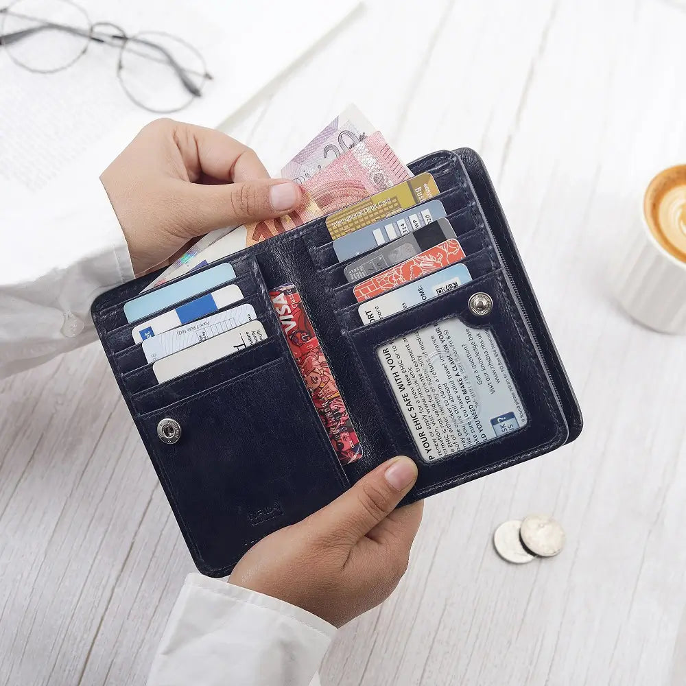 Person holding an open black wallet with cards and money on a light wooden surface.