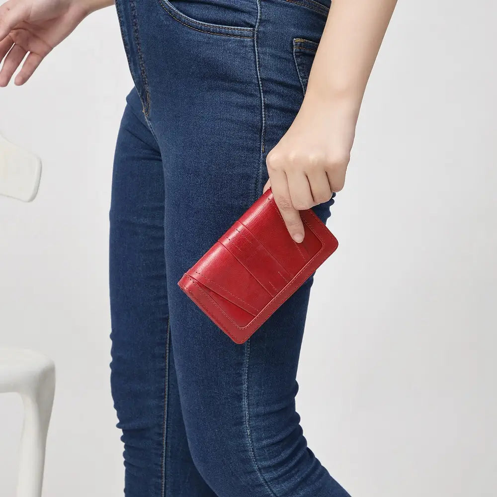 Person holding a red wallet with blue jeans on a light gray background