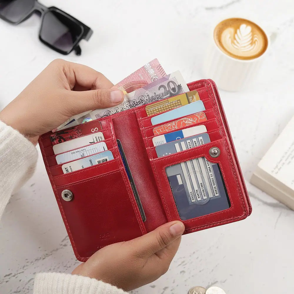 Red wallet with money and cards held by a hand, with a blurred background of a cup of coffee and sunglasses.