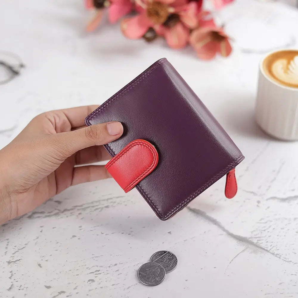 Hand holding a Grape wallet with a red accent on a marble surface with coins and a cup of coffee.