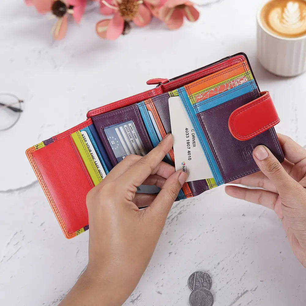 Grape wallet with card slots held by hands on a light surface with flowers and a coffee cup in the background.