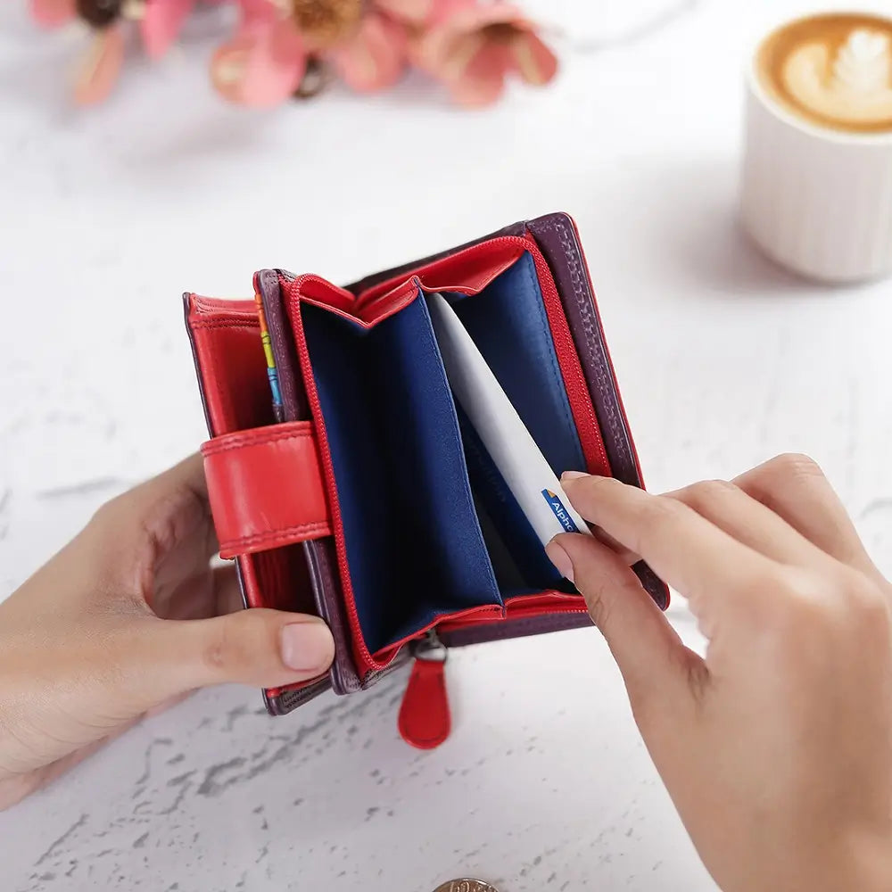 Grape wallet with blue interior held open by hands on a light surface with flowers and a cup in the background.
