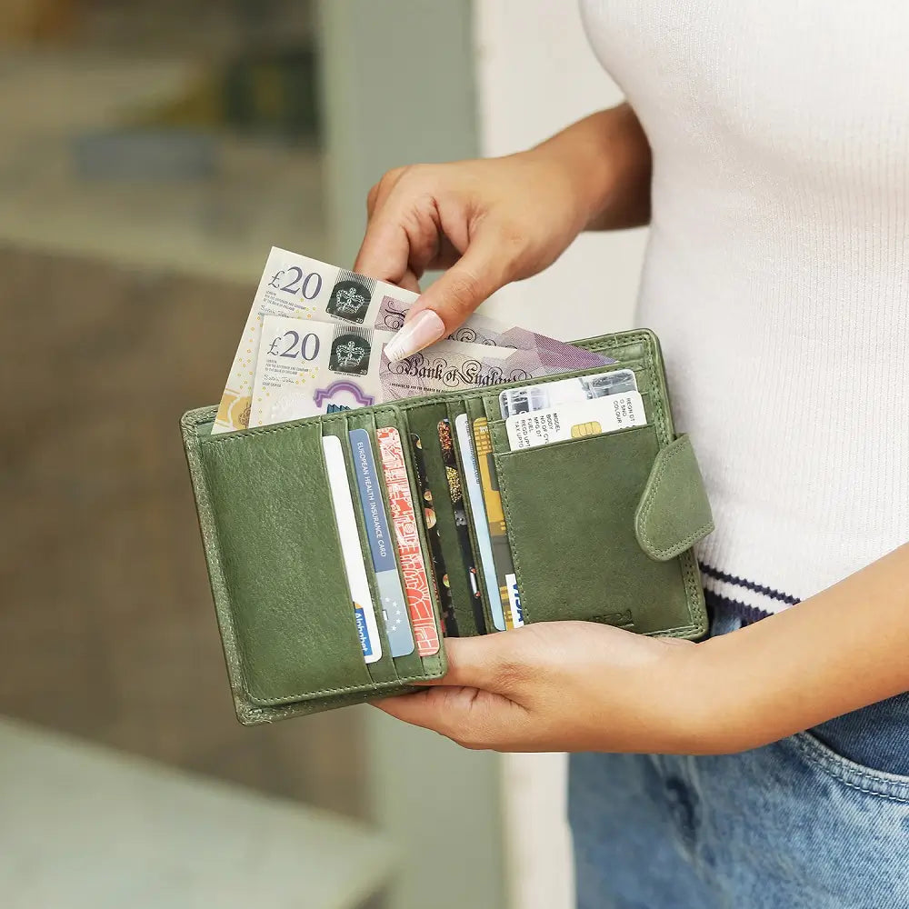 Person holding a green wallet with British currency and cards.