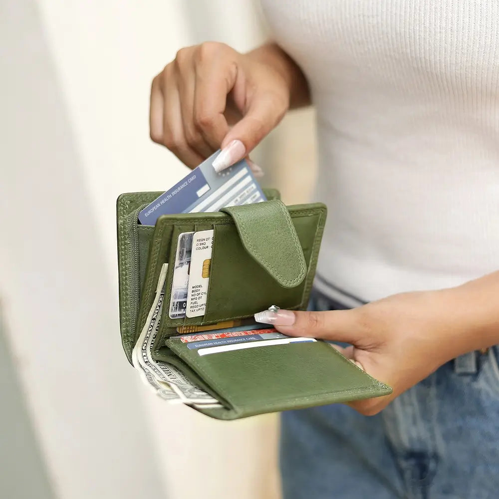Green wallet with cards and money held by a person against a neutral background