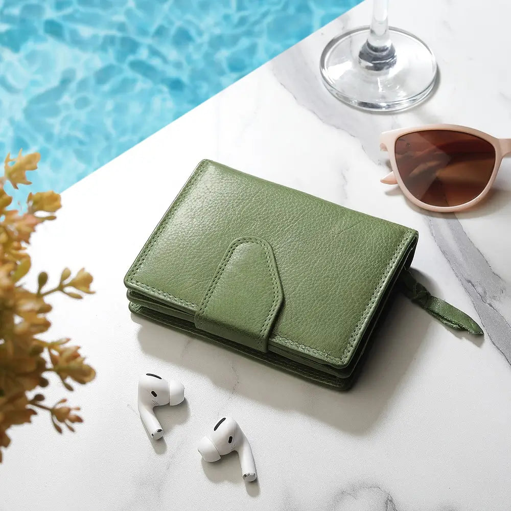 Green leather wallet with white earbuds and sunglasses on a marble surface near a pool.