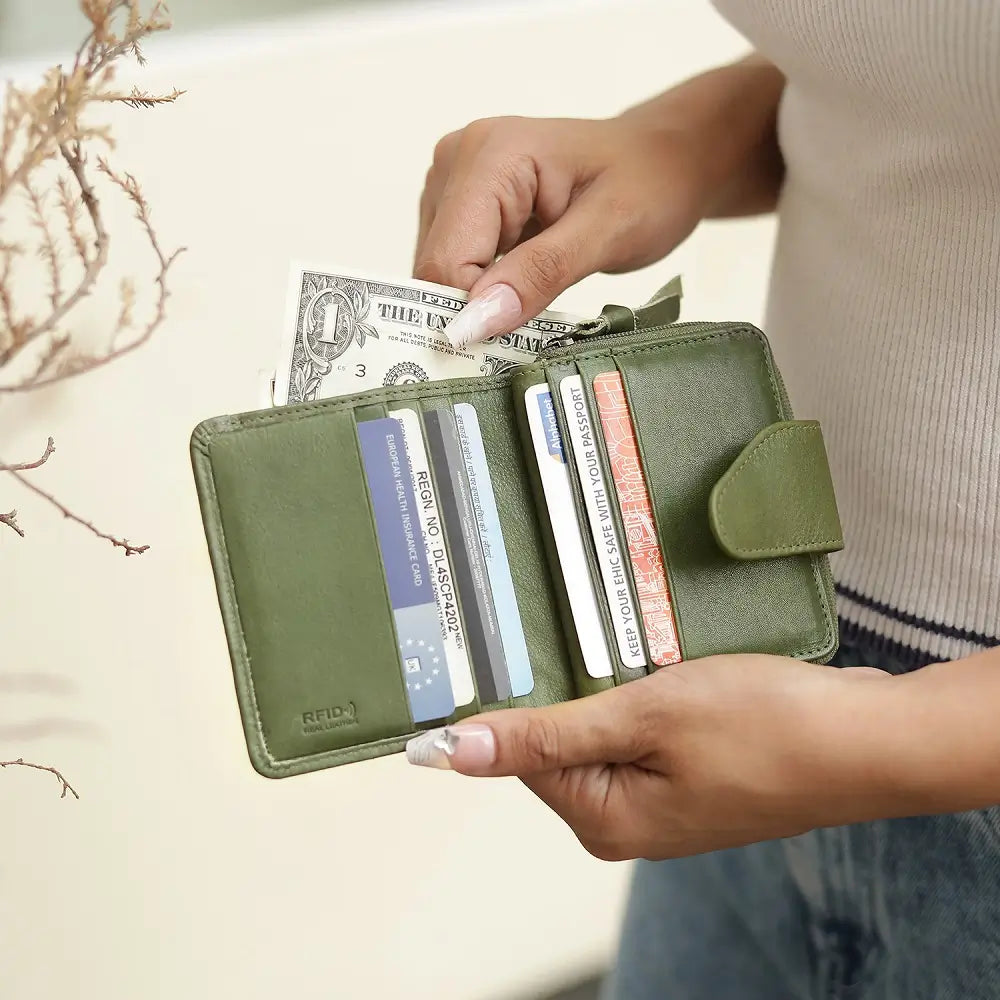 Green wallet with money and cards held by a person against a neutral background