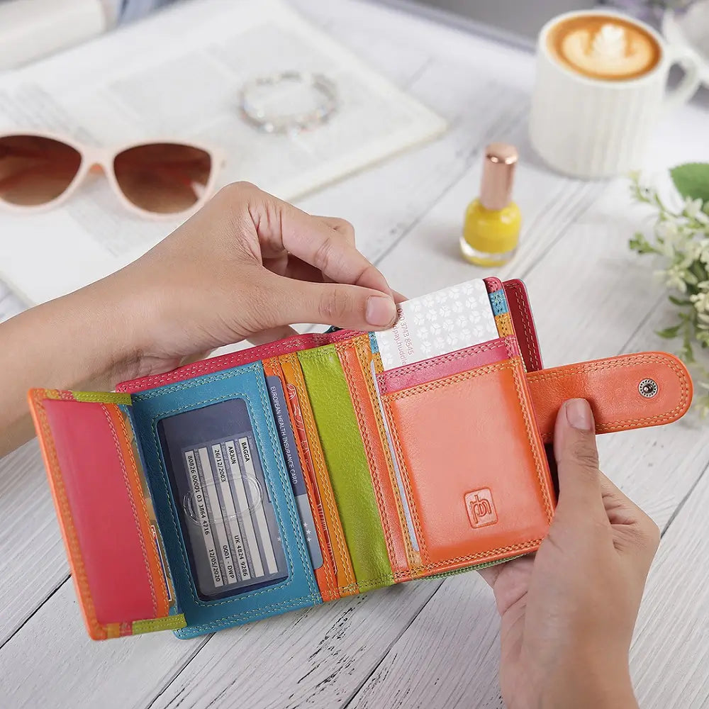 Green wallet with card slots held by a hand on a wooden surface with sunglasses and a cup of coffee in the background.