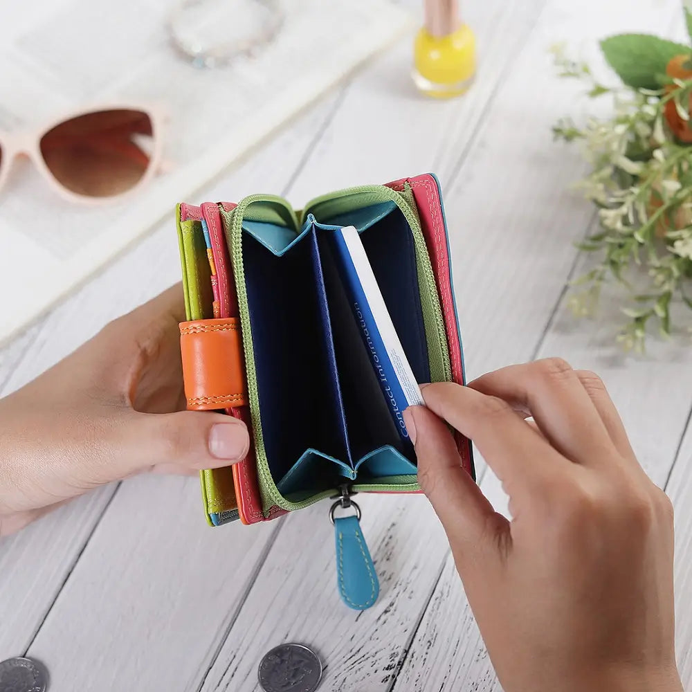 Green wallet with multiple card slots held by hands on a light wooden surface.