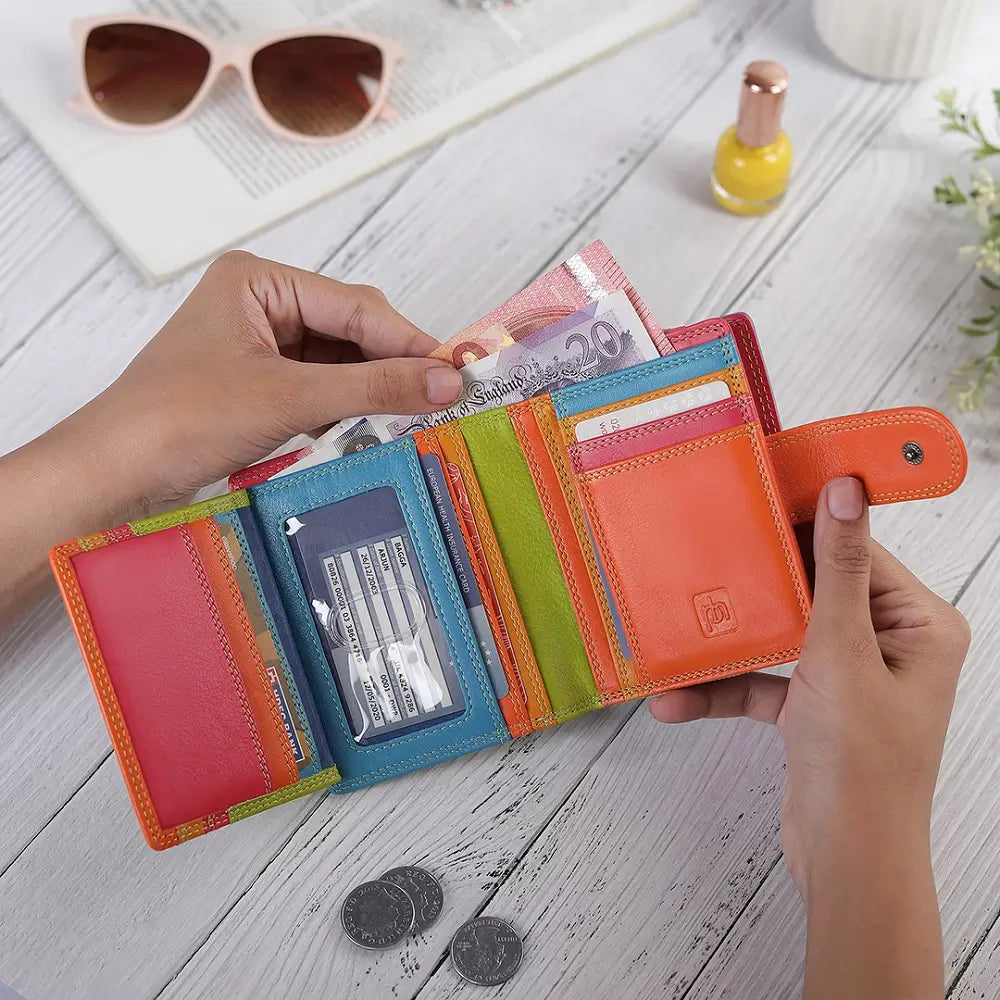 Red wallet with various cards and money held by hands on a wooden surface.