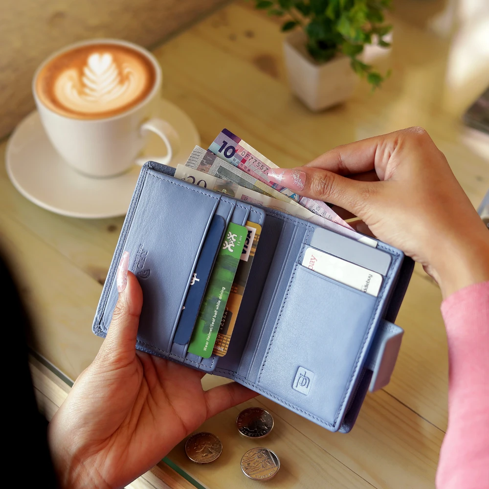 Person holding a blue wallet with money and cards, with a cup of coffee and coins on a table in the background.