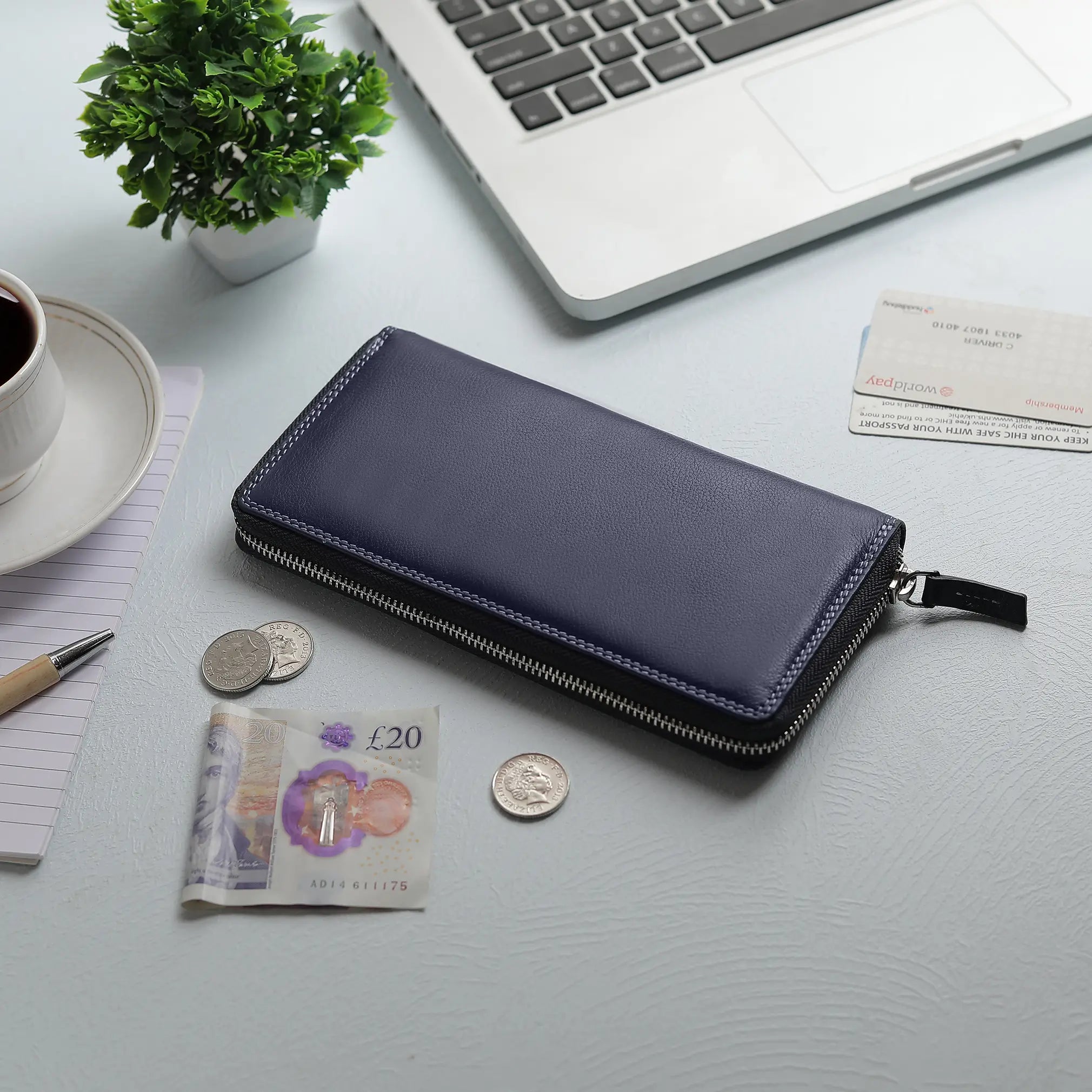 Navy purse on a desk with a laptop, coffee, and currency.