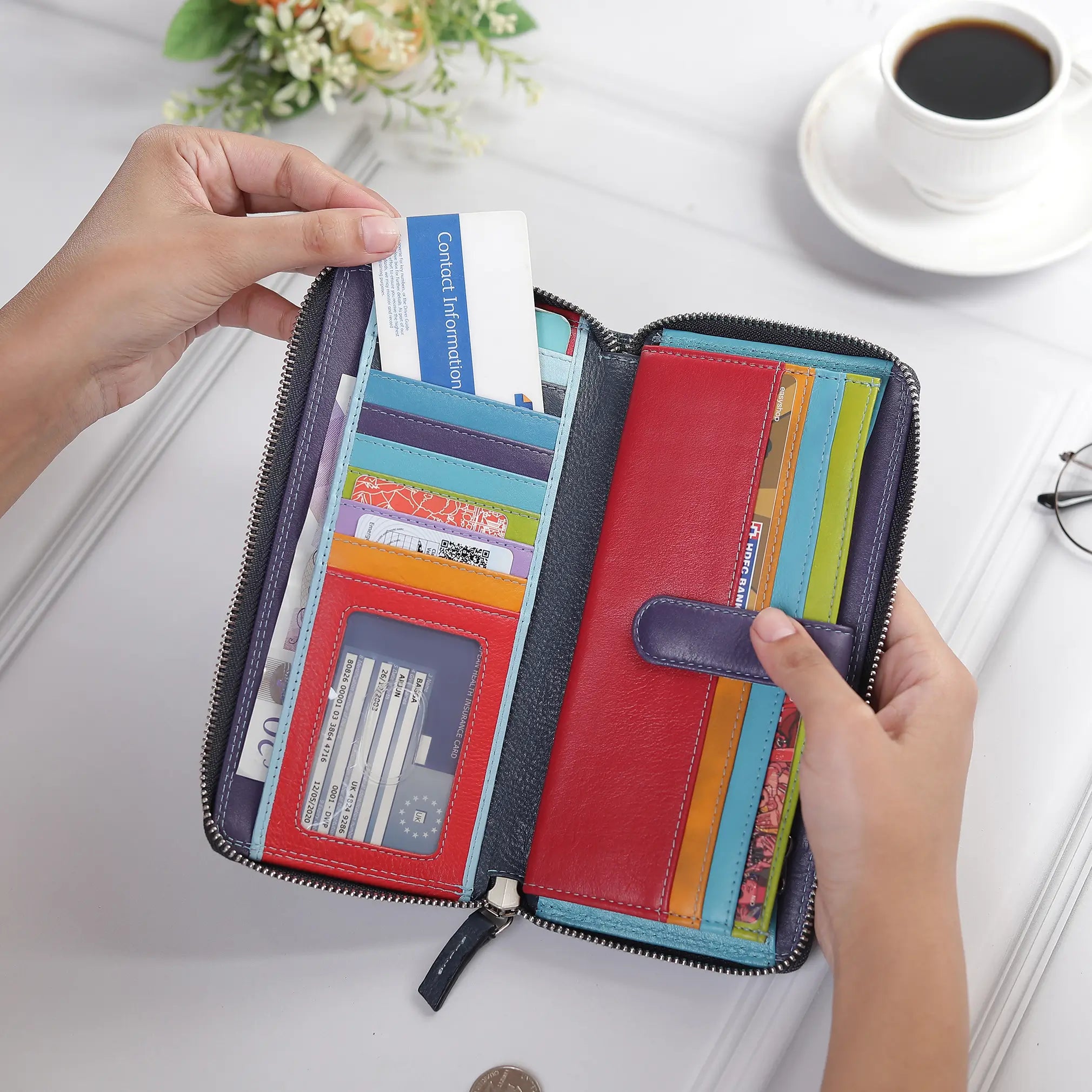 Navy purse with cards and cash held by hands on a light surface with a cup of coffee.