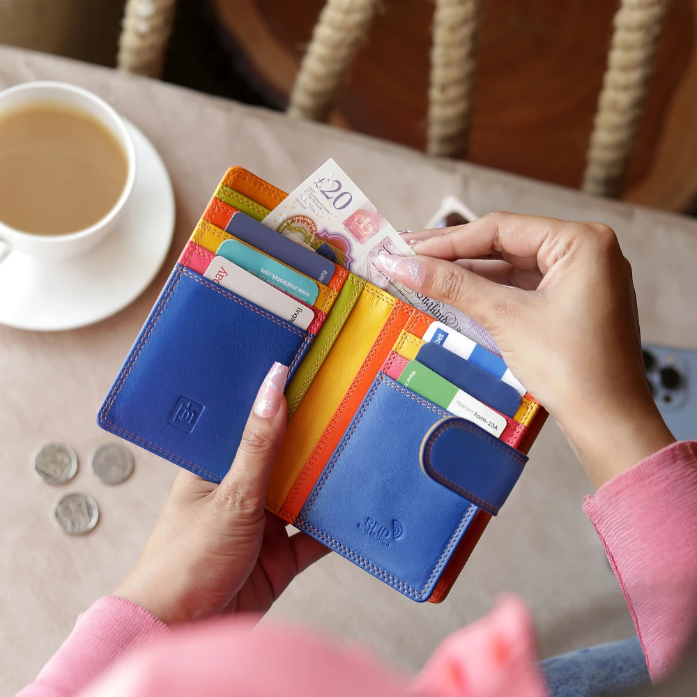 Orange wallet with cards and money held by hands on a table with a cup of coffee.