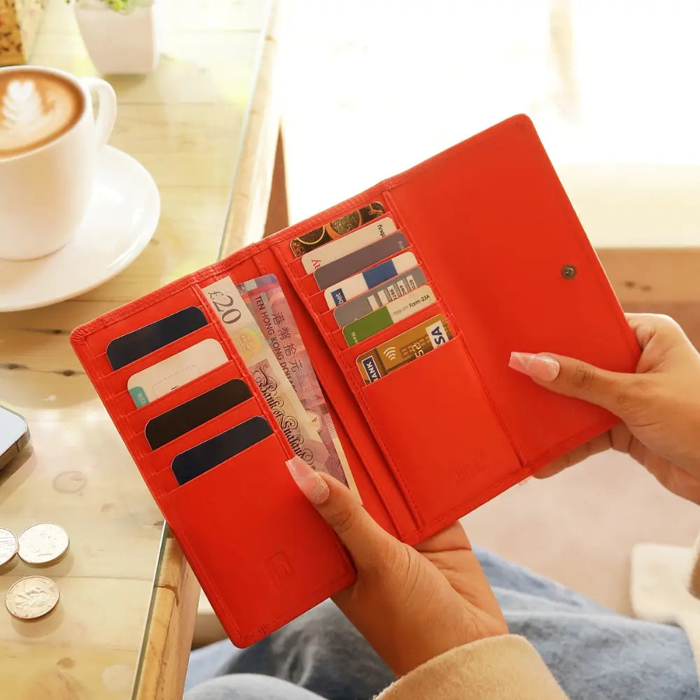 Orange wallet with card slots and cash held by a hand, with a blurred background of a cafe setting.