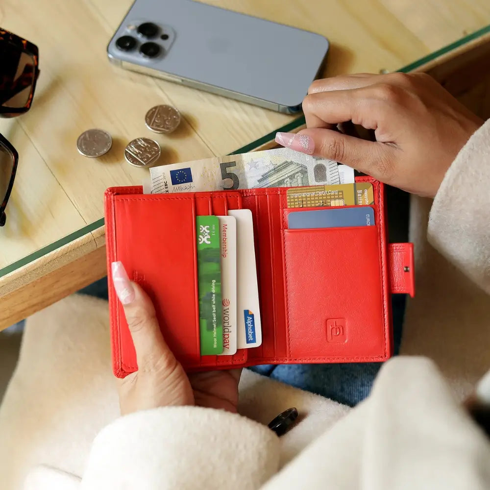 Person opening a red wallet with money and cards on a wooden table.