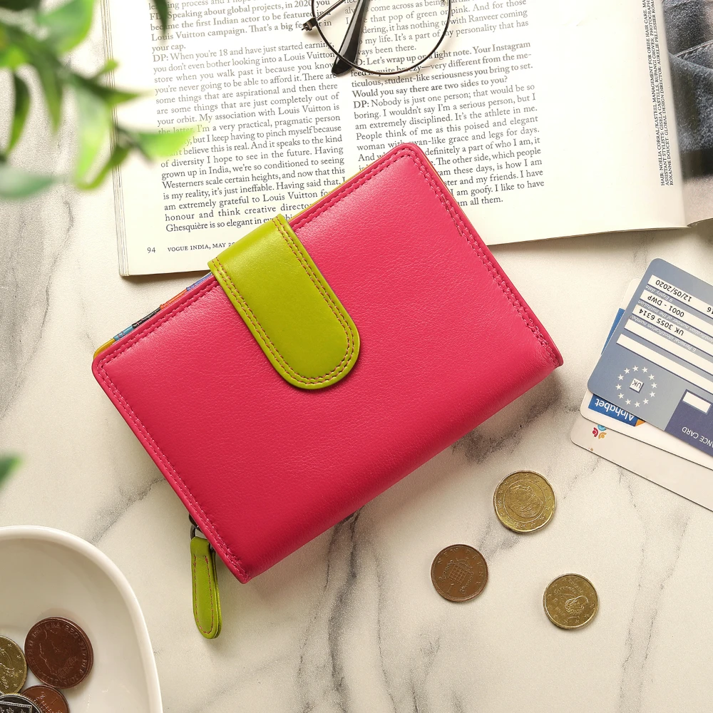 Pink wallet with green strap on a marble surface with coins and cards