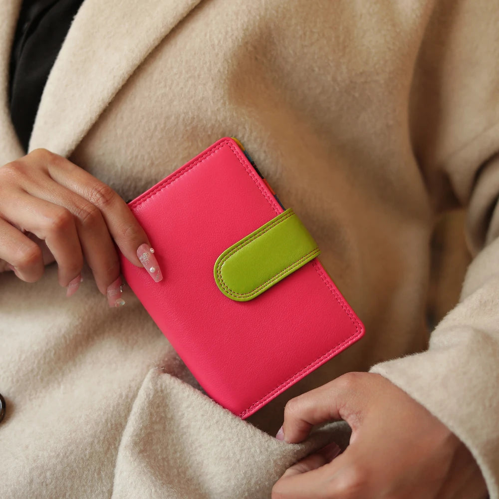 Person holding a pink notebook with a green strap against a beige coat.