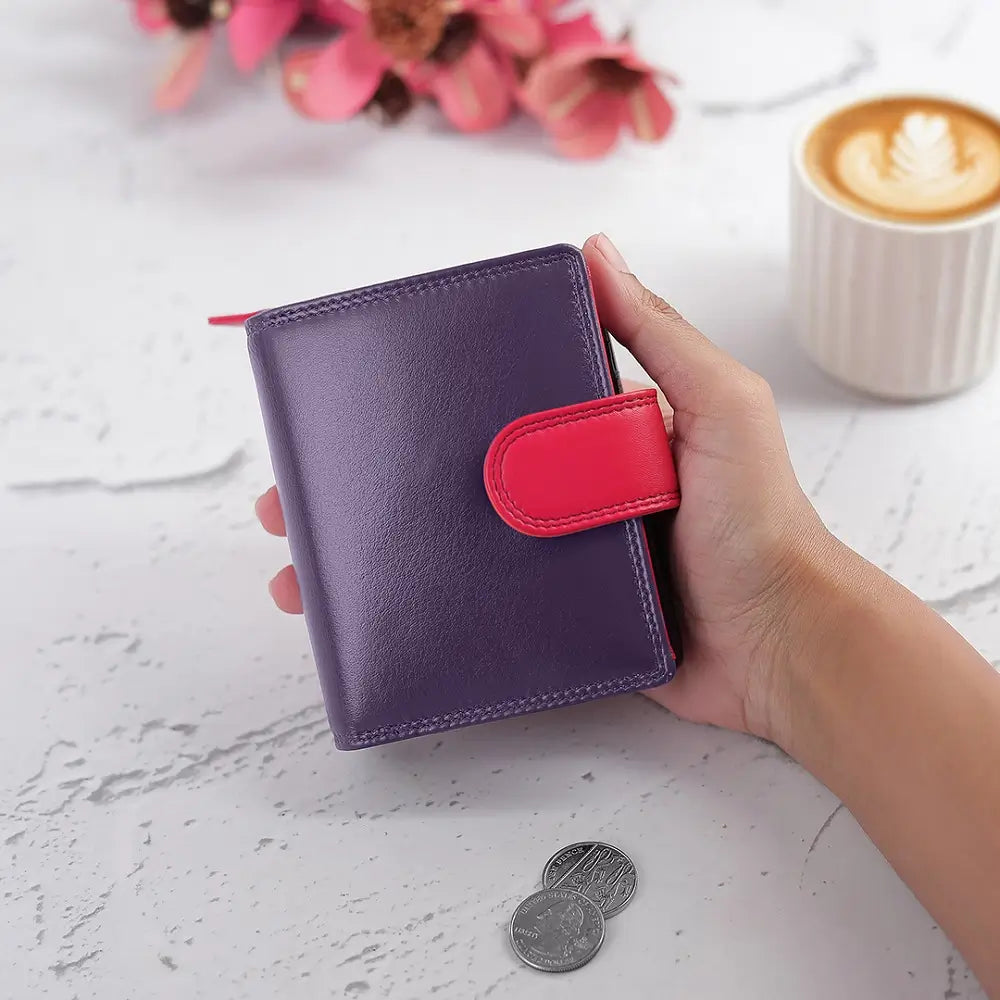 Hand holding a purple wallet with a red flap on a light surface with coins and a cup of coffee.