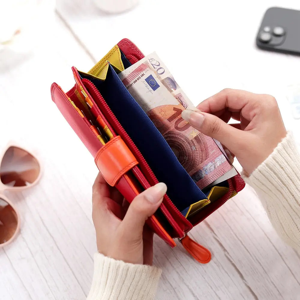 Person holding a red wallet with money and cards on a light surface.