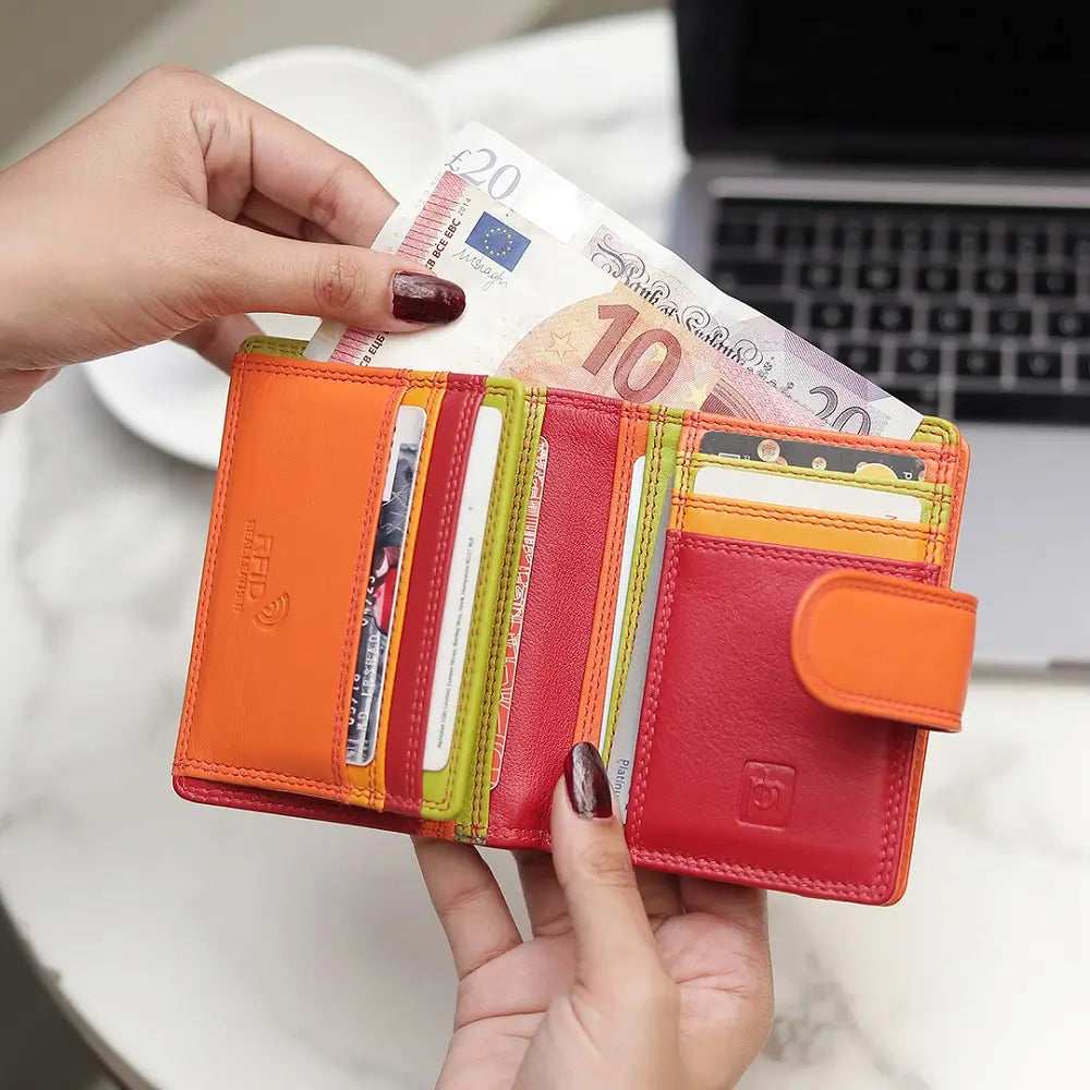Red wallet with money held by a hand, blurred laptop in the background