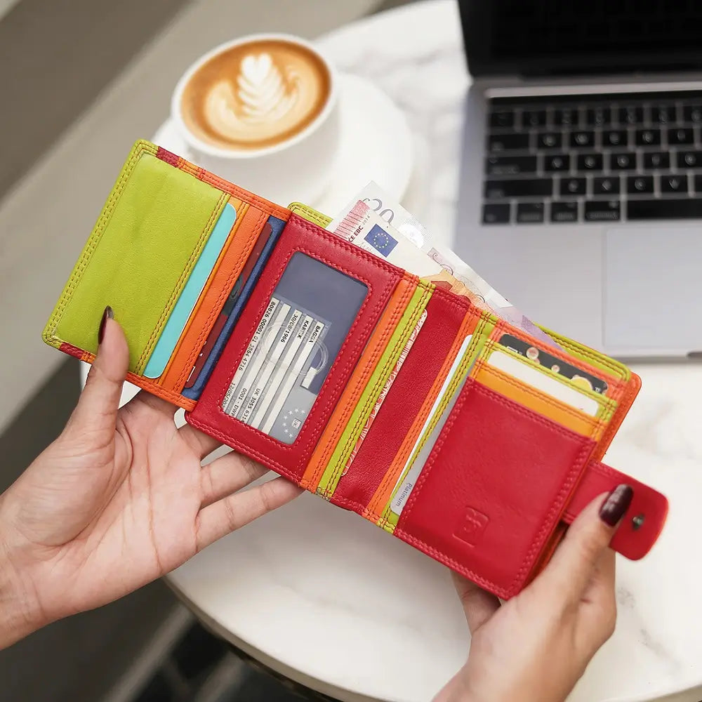 Red wallet with money and cards held by a person, with a cup of coffee and laptop in the background.