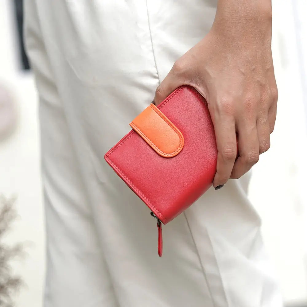 Red wallet with orange flap held by a person wearing white pants.
