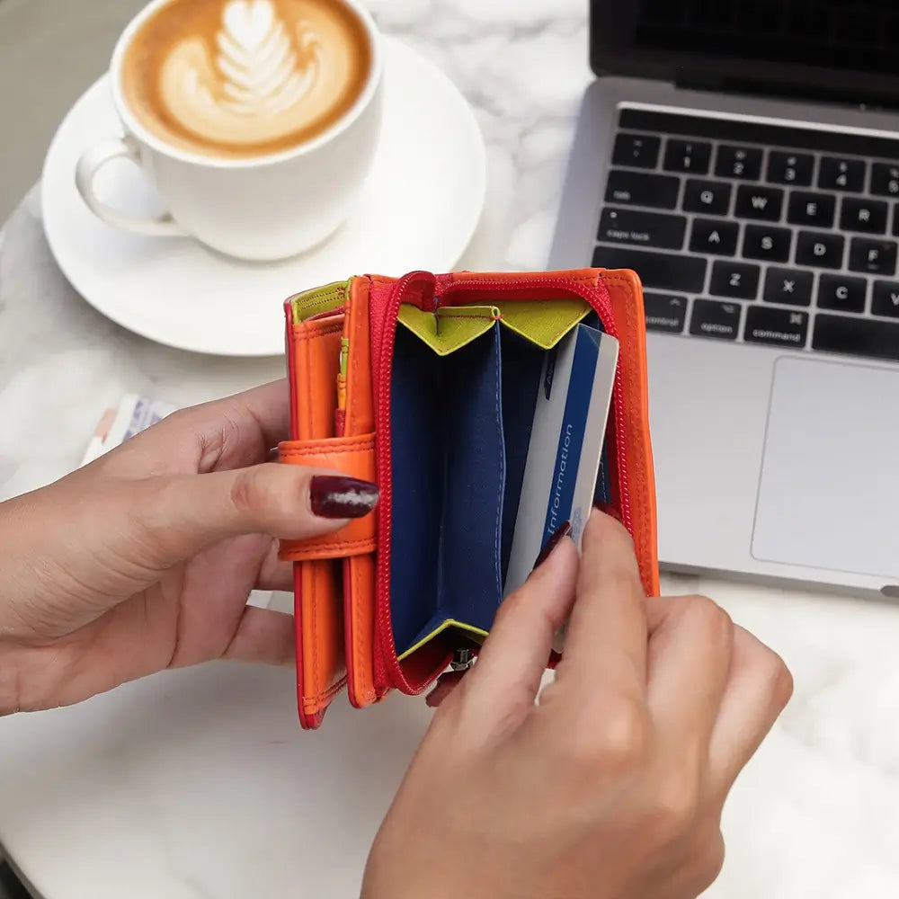 Person holding an orange cardholder with a laptop and coffee in the background