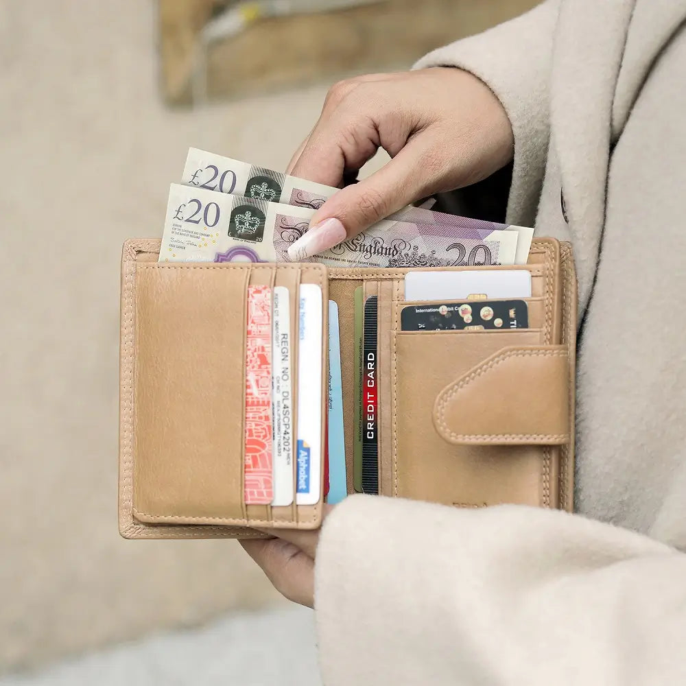 Person holding a sand wallet with money and cards against a neutral background