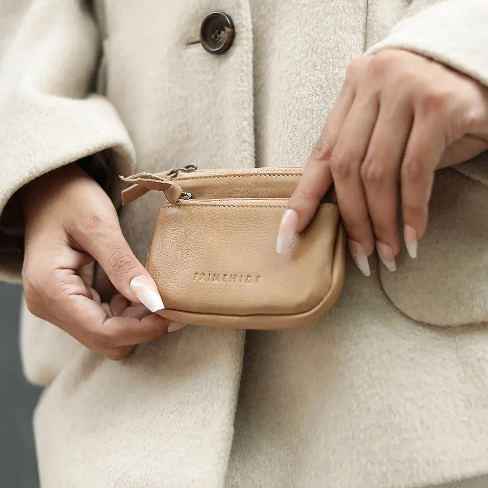 Person holding a small Sand purse with branding against a neutral background.
