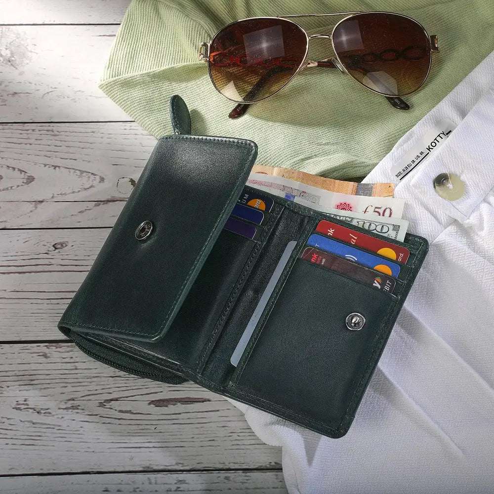 Open Teal wallet with money and cards on a wooden surface with sunglasses and a green shirt in the background.