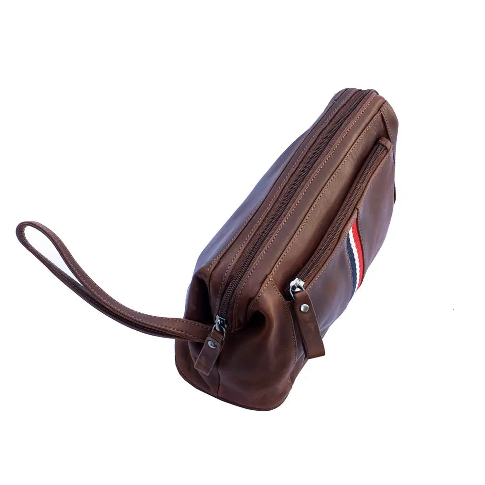 A cognac washbag  with a wrist strap, shown at an angle on a plain white background. It features a diagonal zippered pocket, a vertical zippered pocket with a small red, white, and blue striped accent, and silver-tone metal hardware.