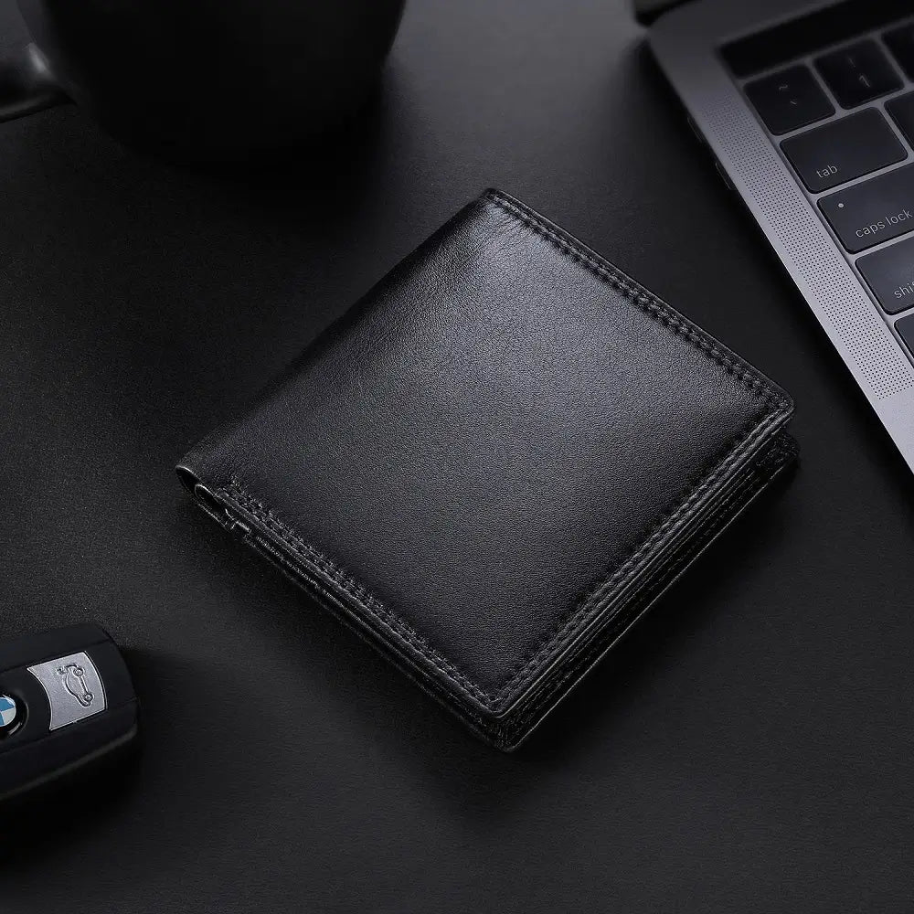 Black leather wallet on a dark surface with a car key and laptop.