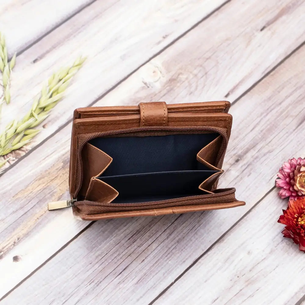 Brown leather wallet with a green strap on a wooden surface with flowers