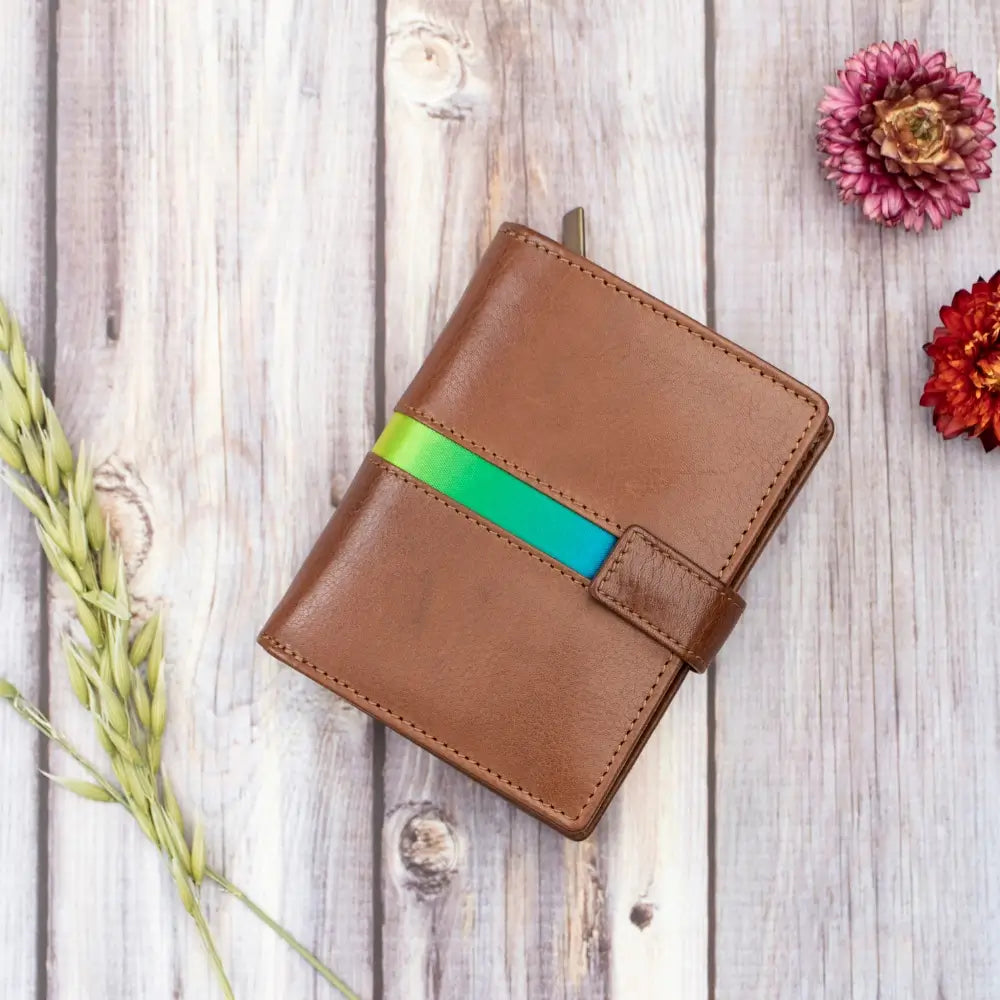 Brown leather wallet with a green strap on a wooden surface with flowers