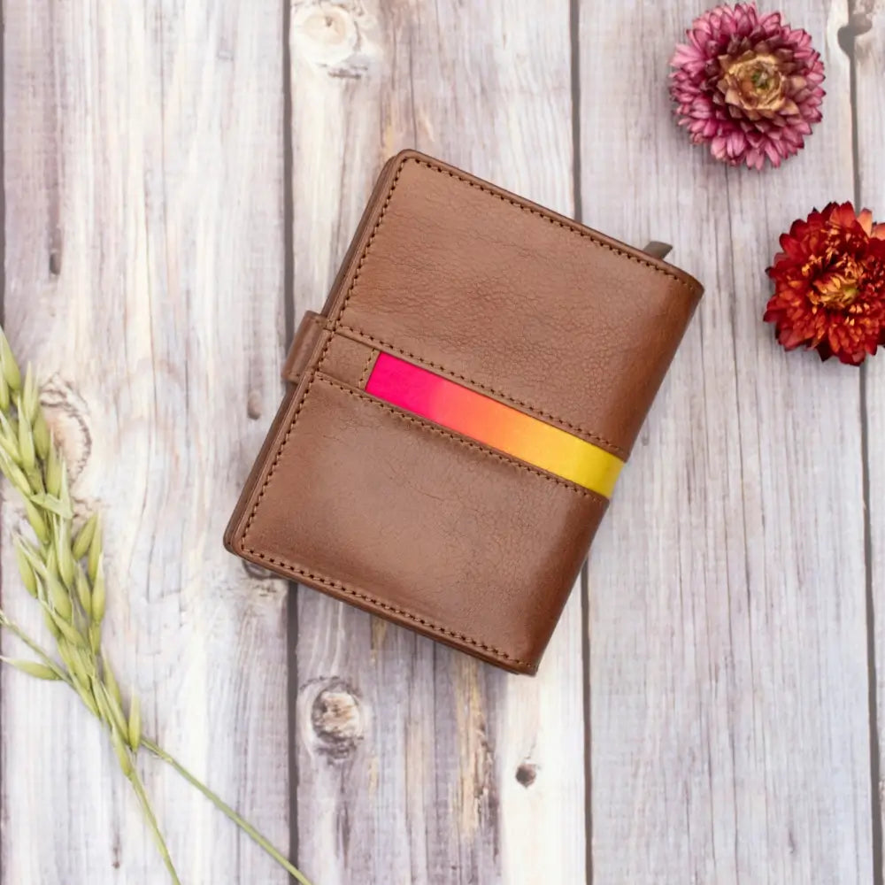 Brown leather wallet with colorful strap on a wooden surface with flowers
