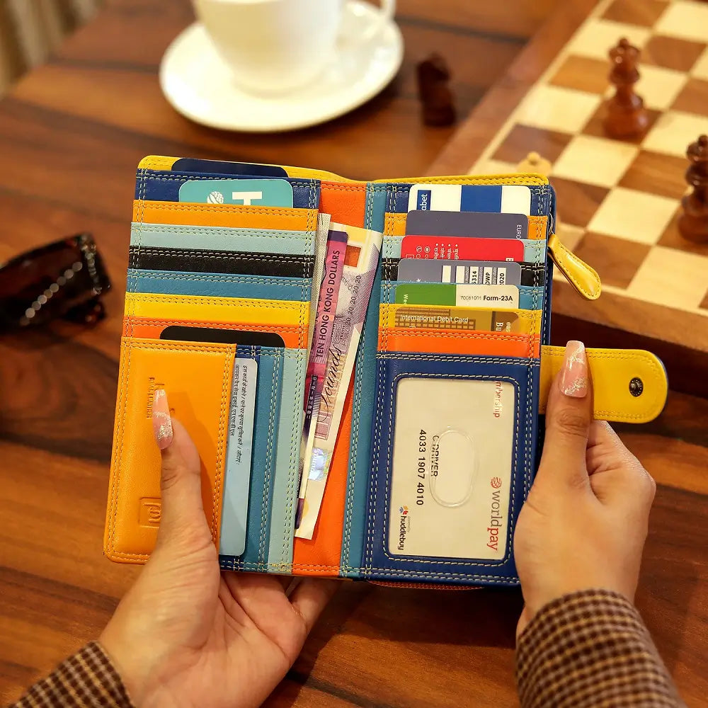 Yellow wallet with multiple card slots held by hands on a wooden table.