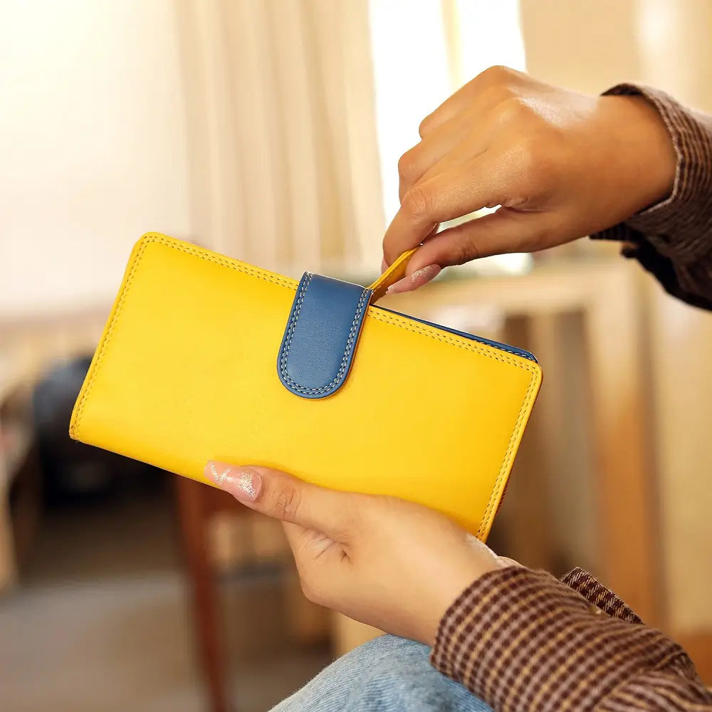 Yellow wallet with blue flap held by a person's hand in a blurred indoor setting