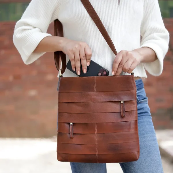 Close-up of a woman placing her phone into the Ridgeback 671 Layered Leather Crossbody Bag, highlighting its front hidden zipped compartment.